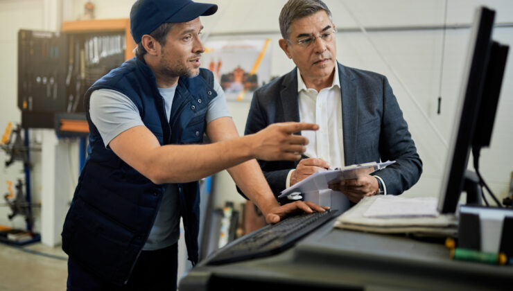 Mid adult manager and car mechanic talking while using computer in auto repair shop.